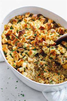 a casserole dish filled with stuffing and topped with a wooden spoon on a white surface