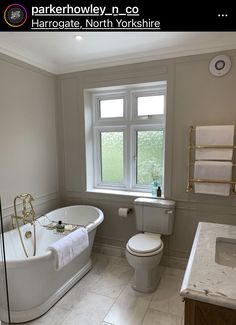 a white bath tub sitting next to a toilet in a bathroom under a window near a sink