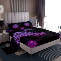 a bed with purple and black comforters in a room next to a lamp on a table