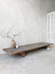 a wooden table sitting in front of a white wall with a vase on top of it