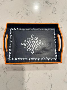 a black and orange tray with an intricate design on the bottom is sitting on a marble countertop