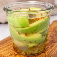 a glass jar filled with sliced avocado on top of a wooden cutting board