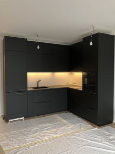 an empty kitchen with black cabinets and white sheets on the floor in front of it