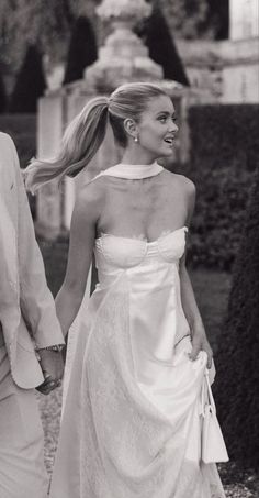 a man and woman are walking down the street holding hands, dressed in white dresses