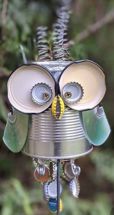 a tin can owl ornament hanging from a tree branch with its eyes open