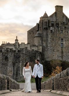 a bride and groom walking in front of an old castle with stone walls on either side