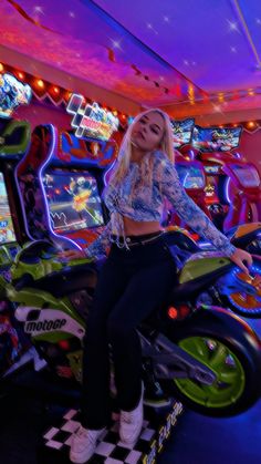 a woman sitting on top of a motor bike in a room filled with arcade machines