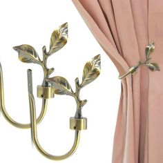 two gold leaves are attached to the curtain rod and hang on a hook in front of pink drapes