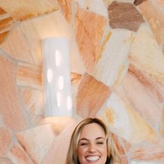 a woman standing in front of a wall holding a cell phone and smiling at the camera