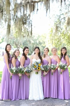 a bride and her bridesmaids pose for a photo in front of an oak tree