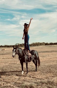 a woman riding on the back of a black horse in a dry grass covered field