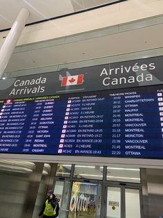 an airport sign showing the arrival and departure times for canada, with a man standing in front of it