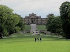 some people are walking around in front of a large building with many trees and grass