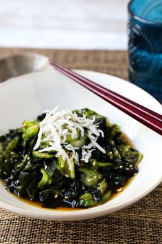 a white bowl filled with food next to chopsticks and a glass of water