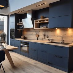 a modern kitchen with blue cabinets and wood flooring is seen from across the room