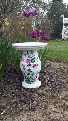 a white vase sitting in the middle of a field with purple flowers growing out of it