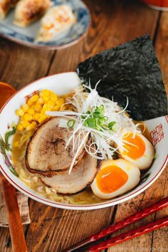 a bowl filled with meat and vegetables on top of a wooden table next to chopsticks