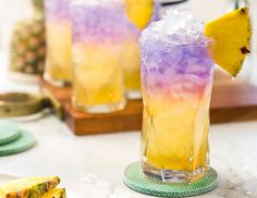 two glasses filled with ice and pineapple on top of a table next to plates