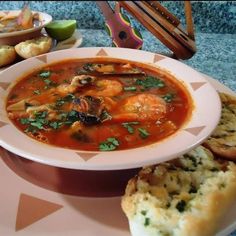 a bowl of soup with shrimp and bread on a table next to other food items