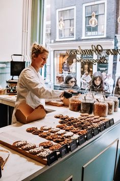 a woman standing behind a counter filled with lots of pastries and donut holes