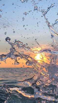 the sun is setting over the ocean with water splashing on it's surface