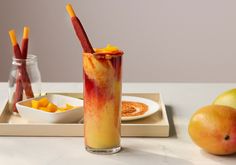 a glass filled with liquid next to some fruit on a plate and two glasses full of orange juice