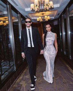 a man and woman in formal wear walking down a hall holding hands with each other