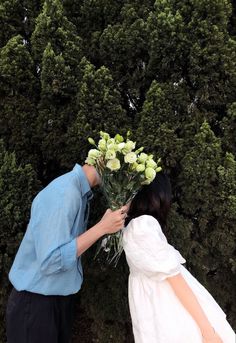 a man and woman kissing each other in front of some bushes with flowers on them