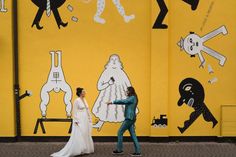 two people walking past a yellow wall with drawings on it