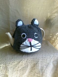 a knitted cat tea cosy sitting on top of a couch