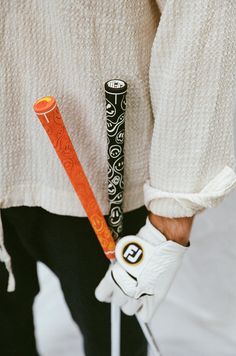 a person wearing white gloves holding two golf clubs and an orange ball in their left hand