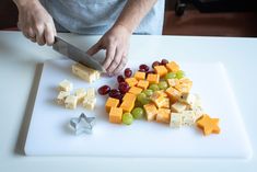 a person cutting up cheese and grapes on a white cutting board with a large knife