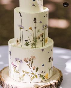 a three tiered wedding cake decorated with wildflowers on a tree stump slice