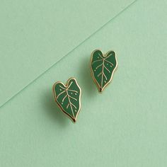 a pair of green leaf shaped earrings sitting on top of a green surface next to each other