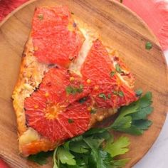 a wooden plate topped with slices of pizza covered in grapefruit and parsley