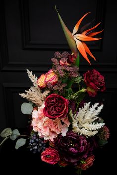 an arrangement of flowers and foliage in front of a black door with a bird of paradise on it