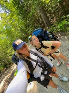 two women hiking in the woods with backpacks on their back and one woman taking a selfie