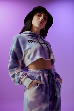 a woman wearing a tie dye hoodie and sweatpants in front of a purple background