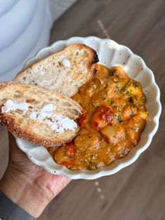 a person is holding a bowl of food with bread in it and there are two pieces of bread sticking out of the bowl