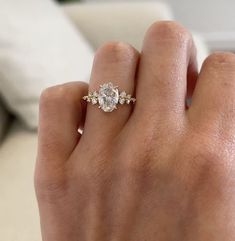 a woman's hand with a diamond ring on top of her finger, in front of a couch