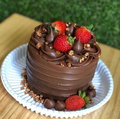 a chocolate cake topped with strawberries on top of a white plate next to a wooden table