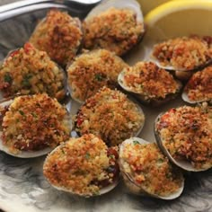 an assortment of cooked clams on a plate with lemon wedges and parmesan cheese