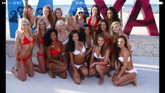 a group of beautiful women in bikinis posing for a photo on the beach with large letters behind them