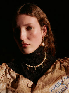 a woman in a black dress with pearls on her neck and gold jewelry around her neck