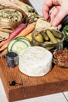 a wooden cutting board topped with different types of vegetables and dips on top of it