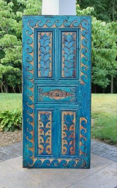 an old door painted blue and gold with ornate designs on the outside, in front of some trees