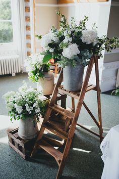 some white flowers are sitting in buckets on a wooden steplade next to a window