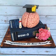 a graduation cake made to look like a brain on top of some books and flowers