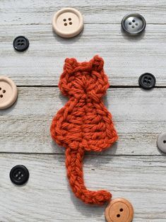 an orange crocheted cat sitting on top of wooden floor next to button holes