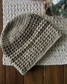 two crocheted dishcloths sitting on top of a wooden table next to a jar of rocks